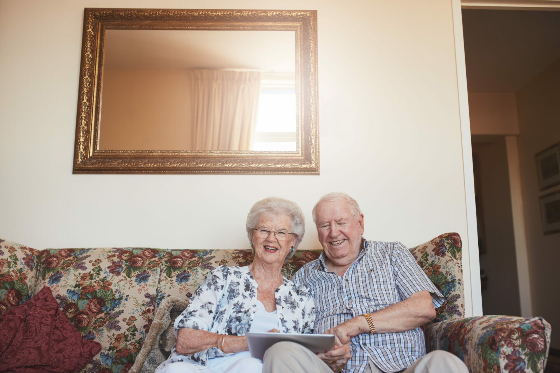 Portrait of smiling senior man and woman sitting together with a digital tablet. Elderly couple sitting on couch at home with a touch screen computer.